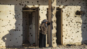 A Syrian Kurdish woman, fleeing from north of Aleppo, stands leaning on a bullet-riddled wall upon arriving in Tabqa, on the western outskirts of Raqa, on December 4, 2024.
