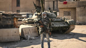 A rebel fighter poses in front of an abandoned tank in the town of Adra on the northeast outskirts of Damascus on December 16, 2024.