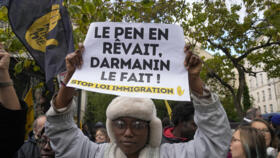 A protester holds a paper reading: "Le Pen dreamed of it, Darmanin does it" during a demonstration in front of the Senate in Paris, Monday, November 6, 2023.
