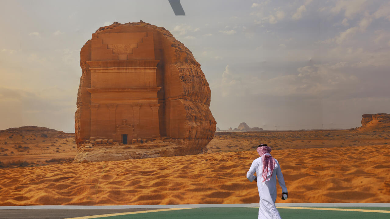 A COP16 delegate walks past a giant poster of a Saudi archaeological site at the start of the UNCCD talks.