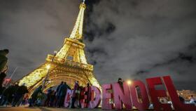 Visitors walk past letters reading "Noël" in front of the Eiffel Tower on December 23, 2023.