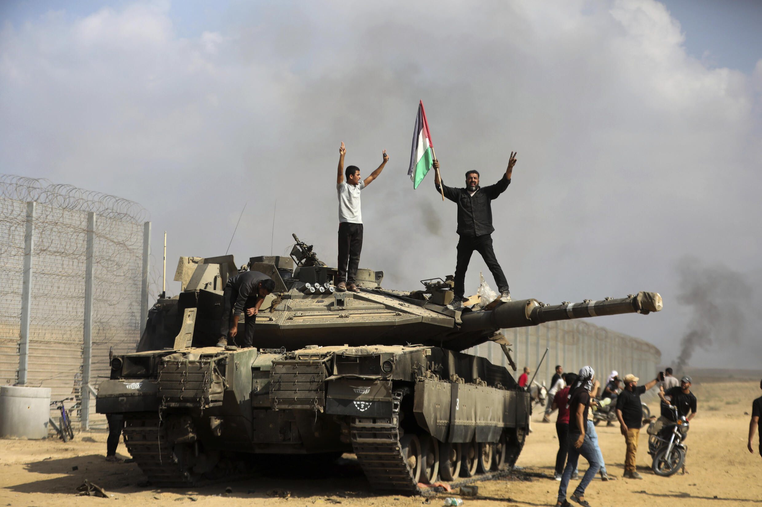 Palestinians wave their national flag and celebrate on a destroyed Israeli tank east of Khan Younis in the southern Gaza Strip on Saturday, Oct. 7, 2023.