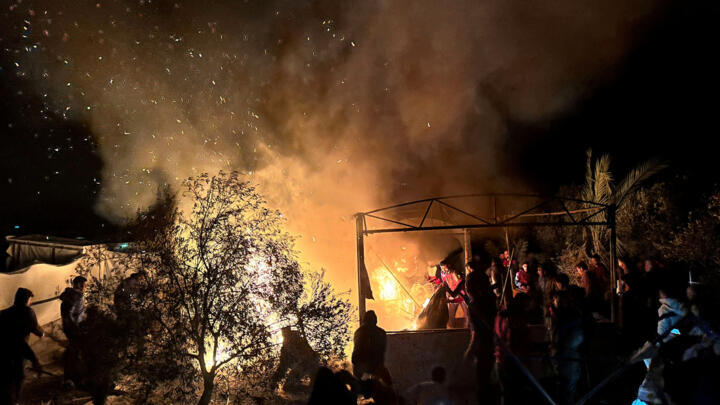 El humo se eleva mientras la gente permanece de pie en un campamento de tiendas de campaña para personas desplazadas, después de un ataque israelí, según los médicos, en medio del conflicto en curso entre Israel y Hamás, en Khan Younis, sur de la Franja de Gaza, 22 de diciembre de 2024.